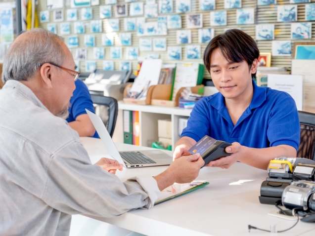 Customer service Asian worker or staff at office counter area receive credit card for payment from senior man. Concept of good service for customer support business system.