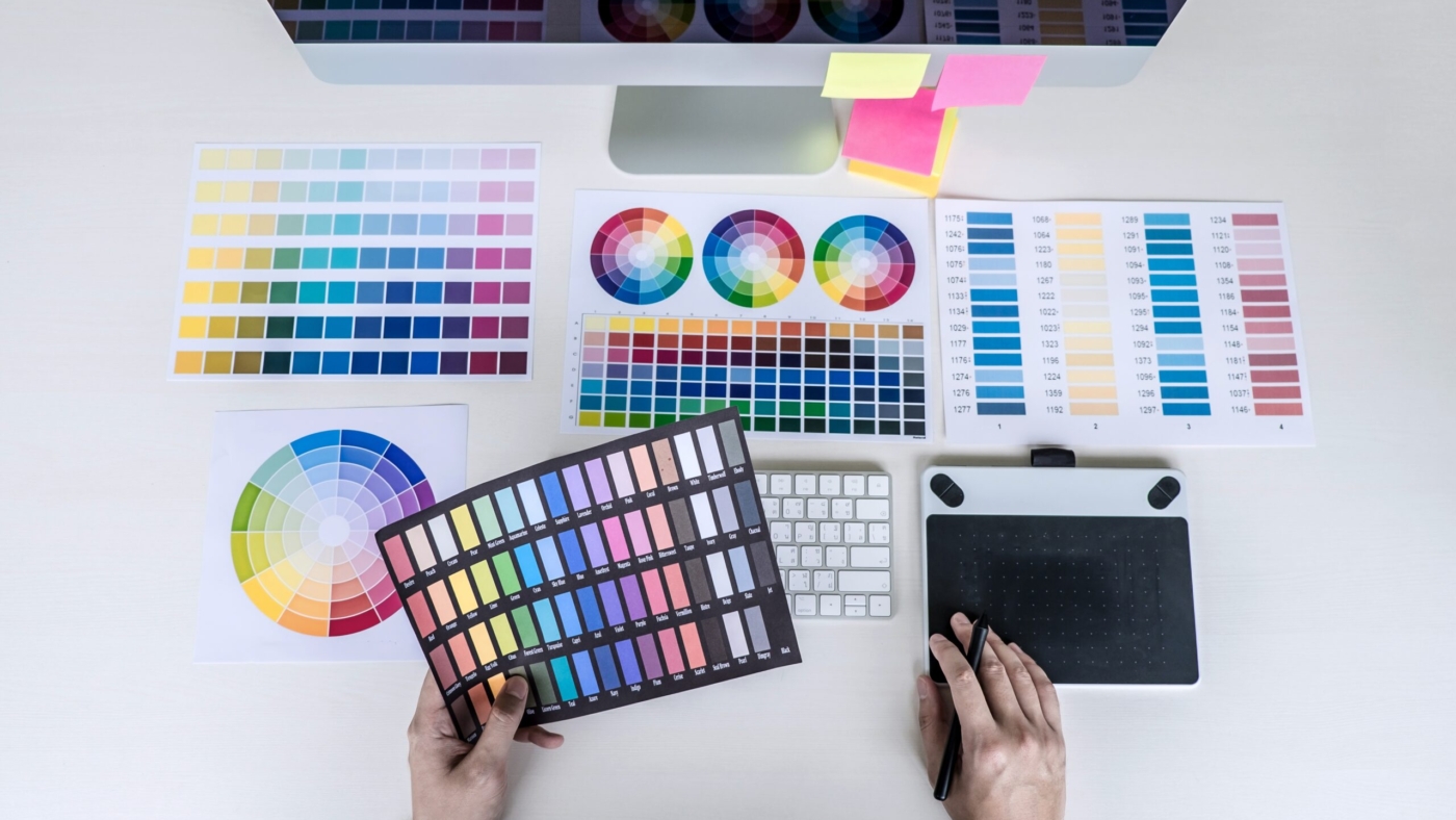 Male creative graphic designer working on color selection and color swatches, drawing on graphics tablet at workplace with work tools and accessories, top view workspace.